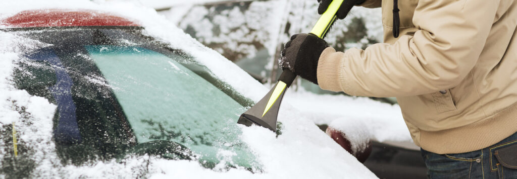 cleaning off a windshield covered in snow